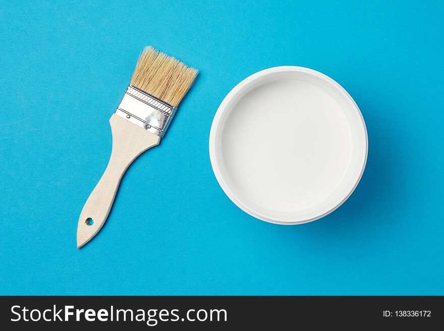 Brush and paint can with white color on a blue background, closeup