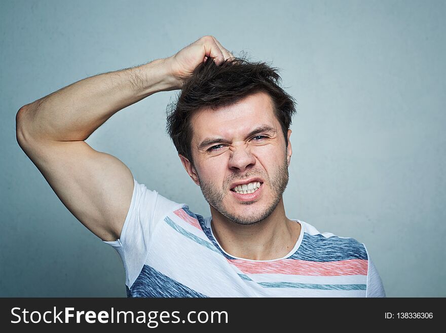Portrait of frustrated young man pulling his hair on a gray wall background