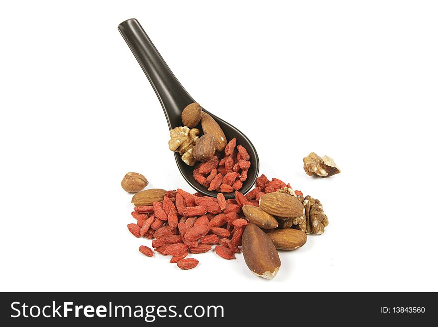 Red dry goji berries with mixed nuts on a small black spoon with a reflective white background. Red dry goji berries with mixed nuts on a small black spoon with a reflective white background