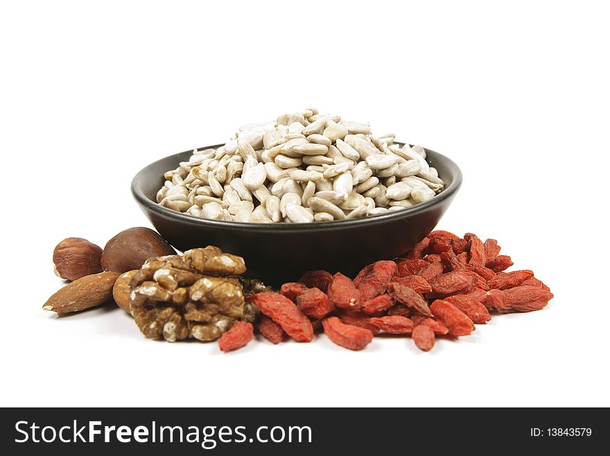 Sunflower seeds in a black bowl with mixed nuts and goji berries on a reflective white background. Sunflower seeds in a black bowl with mixed nuts and goji berries on a reflective white background