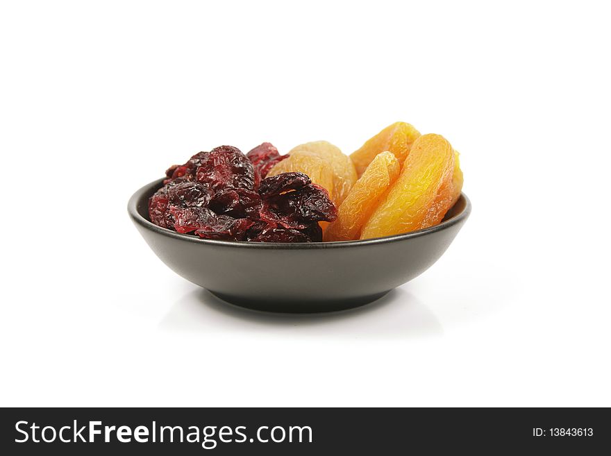 Red ripe dried cranberries and dried apricots in a small black bowl on a reflective white background. Red ripe dried cranberries and dried apricots in a small black bowl on a reflective white background