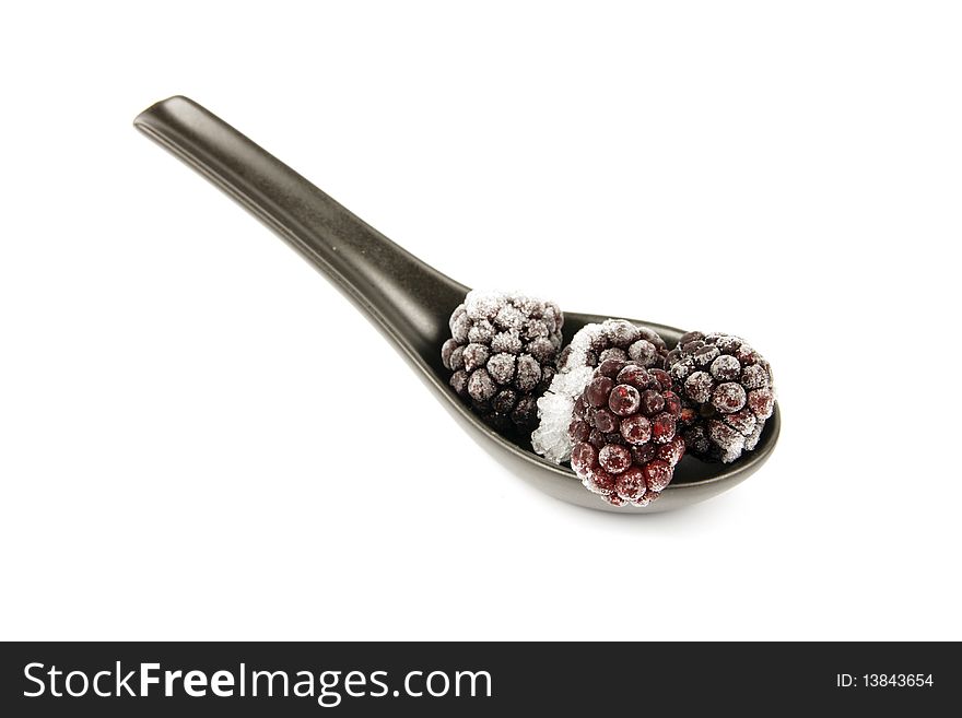 Ripe frozen blackberries on a small black spoon with a reflective white background. Ripe frozen blackberries on a small black spoon with a reflective white background