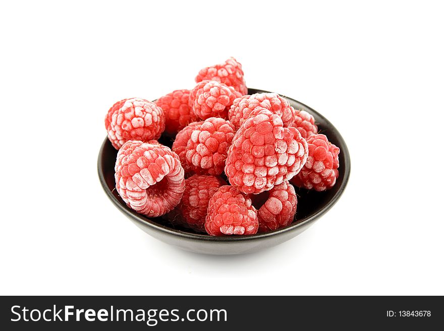 Red ripe frozen raspberries in a small black bowl on a reflective white background. Red ripe frozen raspberries in a small black bowl on a reflective white background