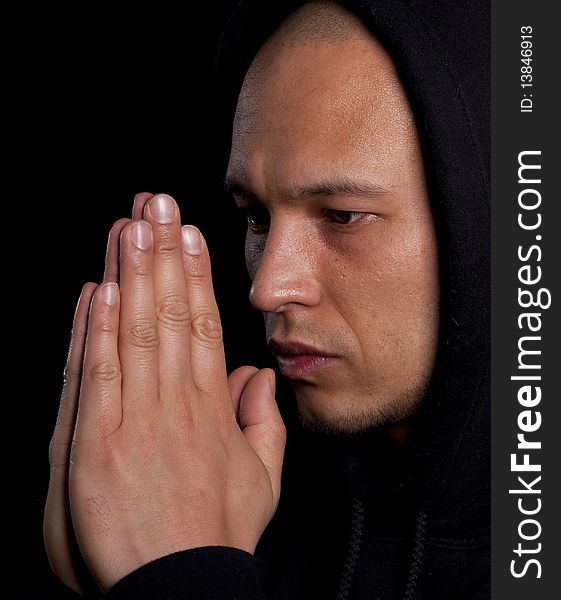 A young asian man with a hoddie is praying over black. A young asian man with a hoddie is praying over black