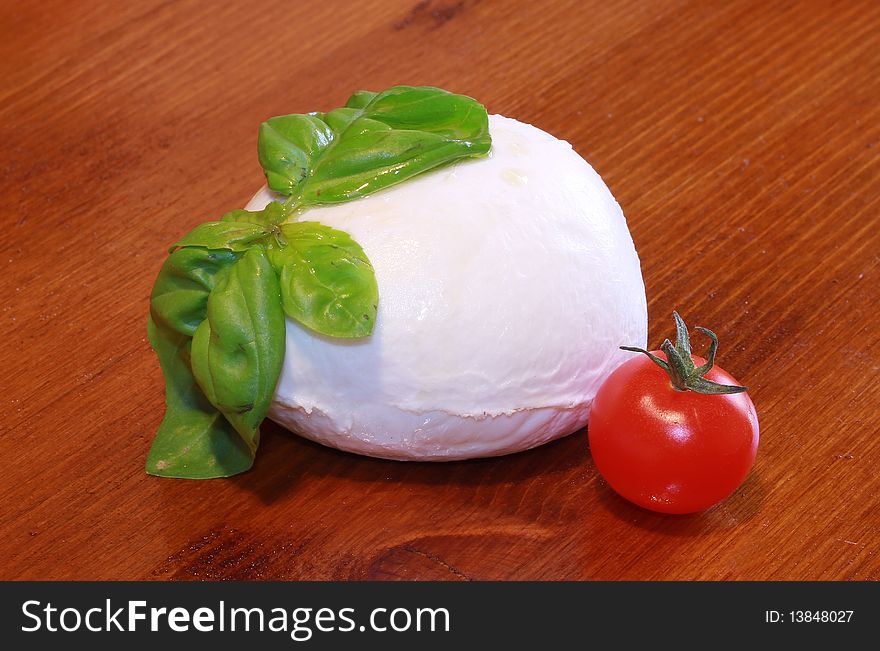 One mozzarella with tomaotoes and basil on wooden table