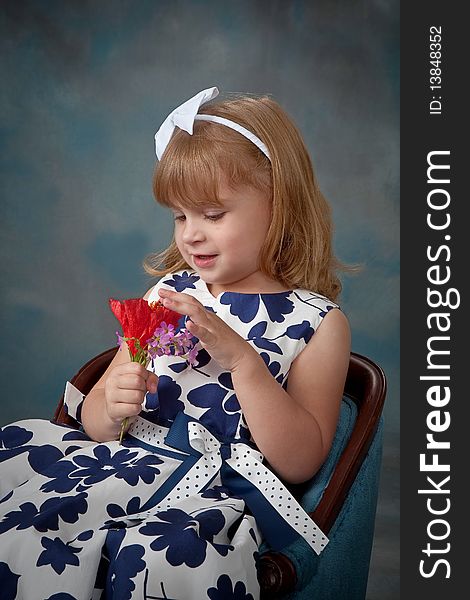 Portrait of a pretty little girl sitting in chair and looking at flowers. Portrait of a pretty little girl sitting in chair and looking at flowers.