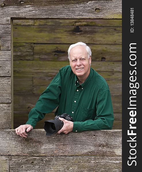 Senior mature man wearing green shirt posing for photograph inside barn window holding a camera. Senior mature man wearing green shirt posing for photograph inside barn window holding a camera.