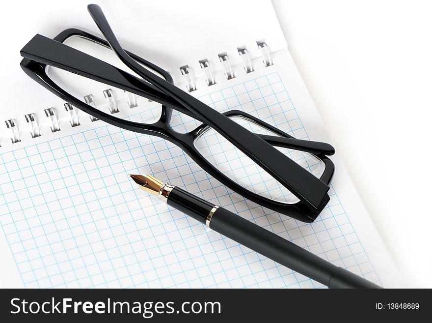 Closeup of fountain pen and black spectacles lying on open spiral notebook. Closeup of fountain pen and black spectacles lying on open spiral notebook