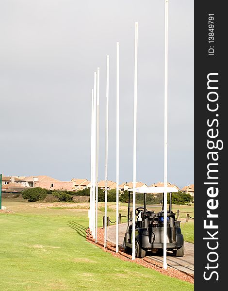 Flag poles on a golf course with a golf car standing by.