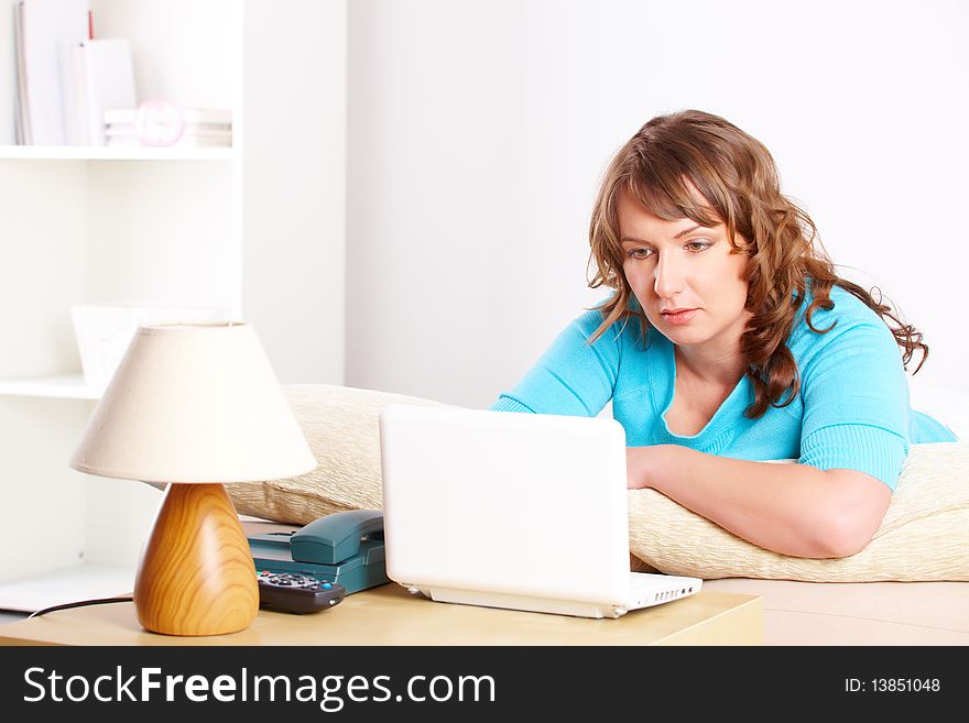 Portrait of a beautiful young woman sitting on sofa and using laptop in home. Portrait of a beautiful young woman sitting on sofa and using laptop in home