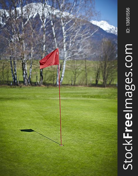 Red flag hole marker at the golf course with mountains in the back