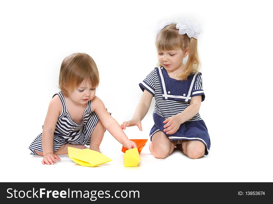 Two young girls playing with paper ships over white