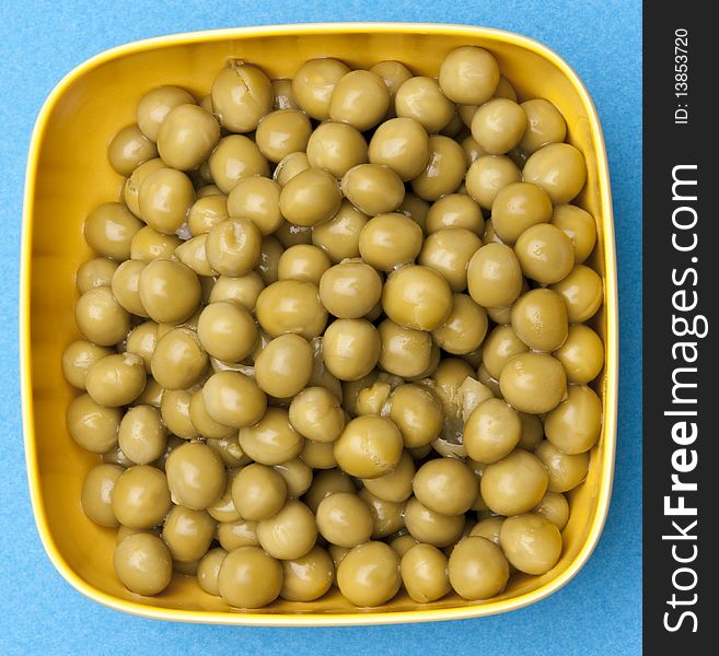 Bowl of canned peas on a vibrant blue background.