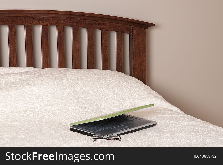 Laptop computer on a bed with a pair of glasses. Working from home concept.