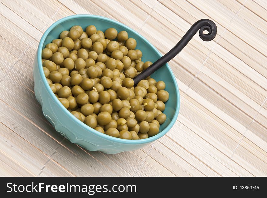 Bowl of canned peas with fork on a bamboo mat background.