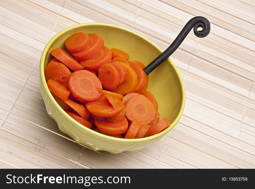 Bowl of canned carrots with fork on a bamboo mat background.