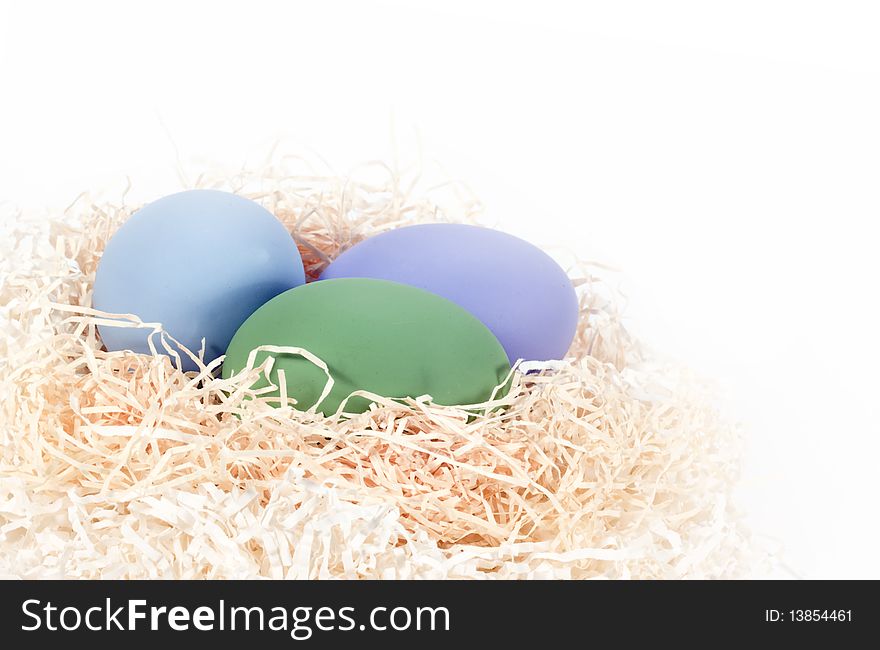 Three colored eggs in shredded paper nest on white background. Three colored eggs in shredded paper nest on white background