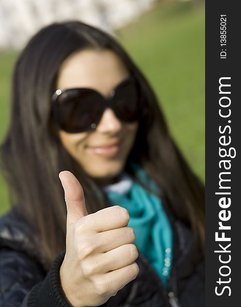 A beautiful young brunette girl in a park sitting on a bench smiling. Thumb sign OK. A beautiful young brunette girl in a park sitting on a bench smiling. Thumb sign OK