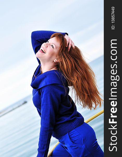 Laughing redheaded girl wearing blue clothes near the sea