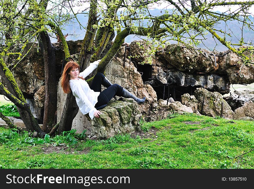 Redheaded gorgeous girl sitting between tree and stone. Redheaded gorgeous girl sitting between tree and stone
