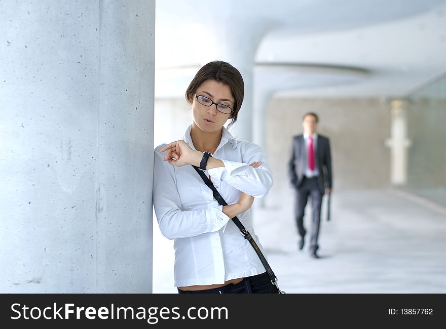A young businesswoman is looking at her watch while a businessman is walking on the background. A young businesswoman is looking at her watch while a businessman is walking on the background.