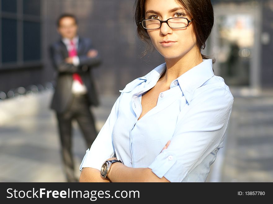 A young businesswoman is looking at the camera while a businessman is standing on the background. A young businesswoman is looking at the camera while a businessman is standing on the background.