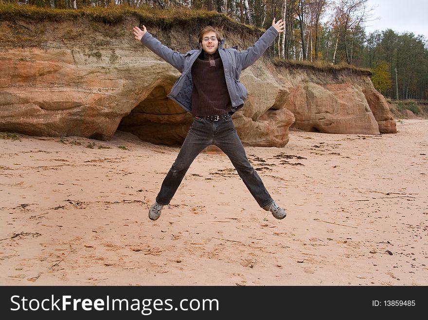 Beautiful young man is jumping on the beach near the caves. Beautiful young man is jumping on the beach near the caves.