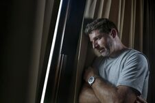 Dramatic Light Indoors Portrait Of Young Sad And Depressed Attractive Man Looking Through Home Room Window Thoughtful And Pensive Stock Image