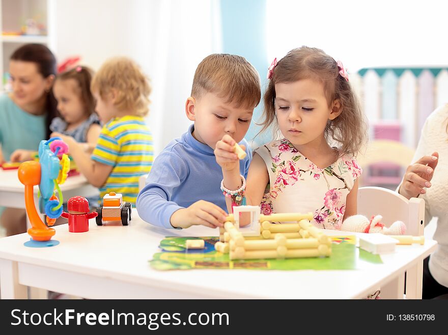 Group of kids playing in kindergarten. Children building toy house with plastic blocks sitting together by the table
