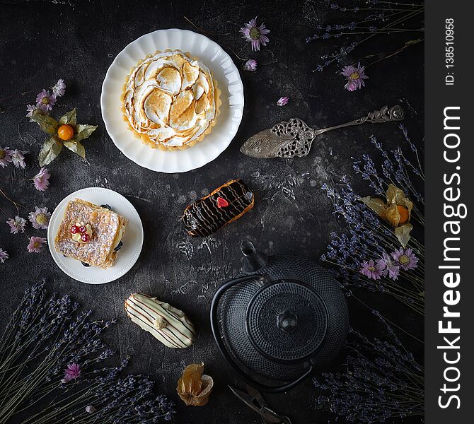 Tea and sweets on a dark background, Mille-feuille, Eclairs, Tart, Decorative with flowers, Top view, Vintage