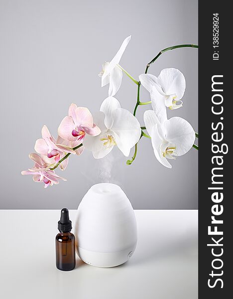 Oil diffuser with glass amber bottle and orchid flowers on white table