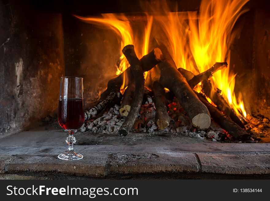 Burning fireplace in the winter season. The firewood burning in fireplace and a glass of wine close-up