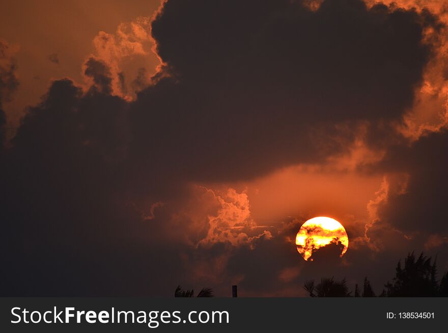 The Rising Sun Seen Against Grey Clouds And An Orange Sky