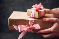 Hands Holding Holiday Gift Boxes Packed In Kraft Paper With Pink Ribbon On Dark Wooden Background Stock Photography