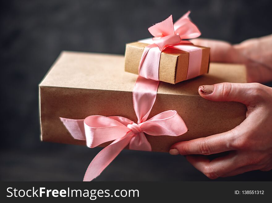 Hands holding gift boxes Packed in Kraft paper with pink ribbon on dark wooden background. Concept holiday card for Valentine`s day and women`s day. Hands holding gift boxes Packed in Kraft paper with pink ribbon on dark wooden background. Concept holiday card for Valentine`s day and women`s day