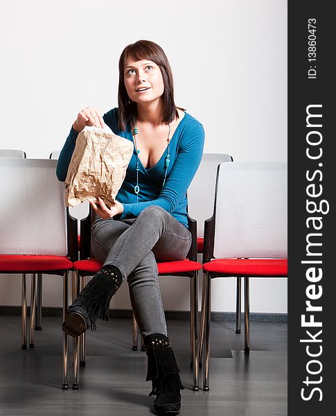 Surprised young woman sitting in cheer row, looking up, holding paper bag. Surprised young woman sitting in cheer row, looking up, holding paper bag