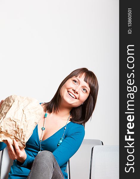 Happy smiling young woman sitting and looking up, holding paper bag. Happy smiling young woman sitting and looking up, holding paper bag