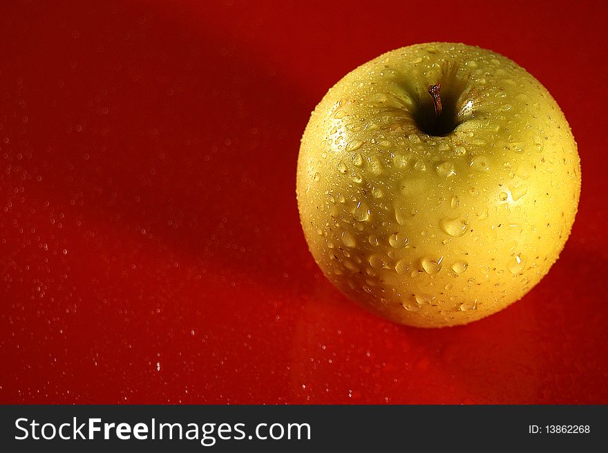 Yellow apple in drop of water on red background (overhand)