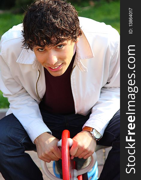 Curly haired young adult man in white, on a playground, outdoor portrait