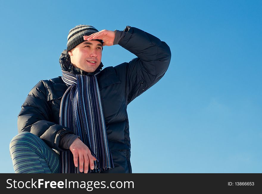The young guy on a background of the sky looks in a distance in the winter