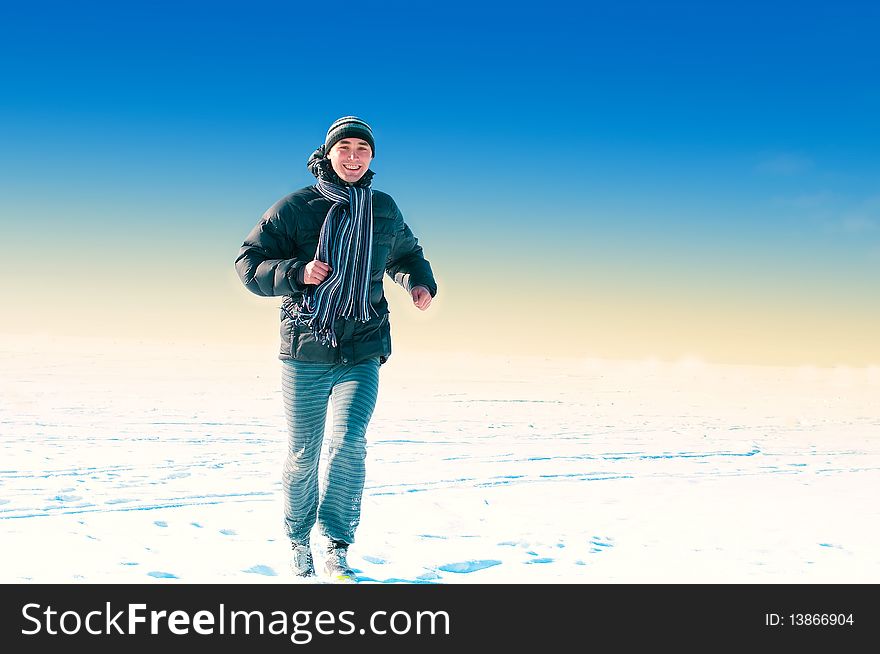 The young guy on a background of the sky looks in a distance in the winter