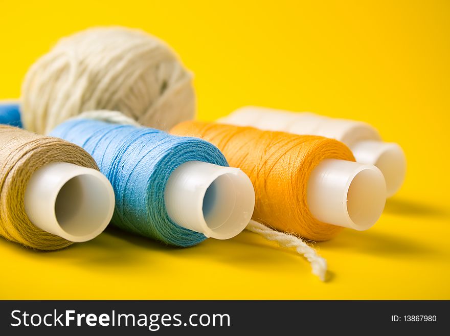 Ball of yarn and spools of thread on a yellow background