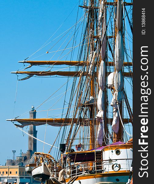 The impressive three masts of an old sailing ship moored in the port of Genoa and on the background the lighthouse symbol of the city