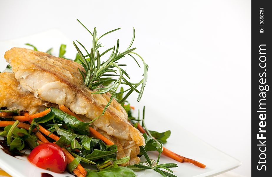 Pan seared fillet of white fish and vegetables on white background