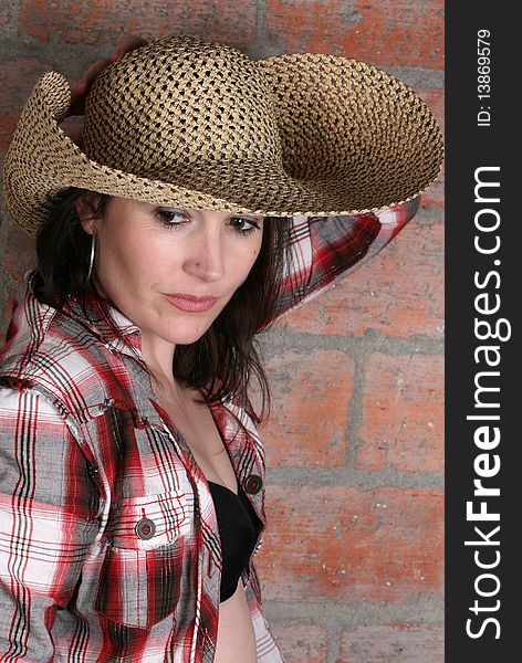 Beautiful brunette woman wearing a broad rimmed hat against a brick wall background