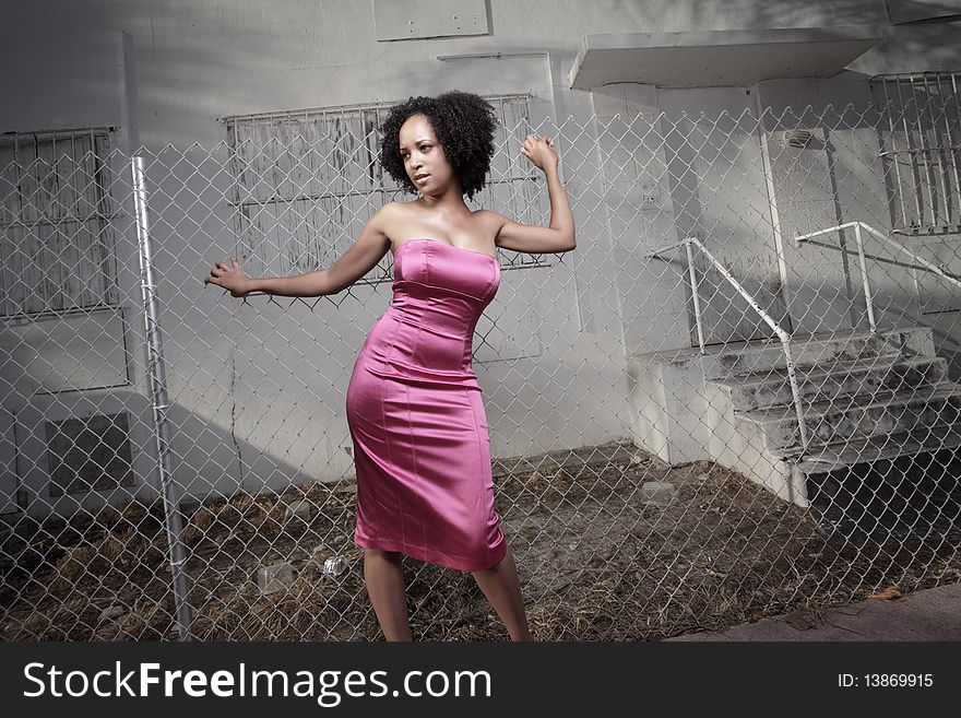 Young woman posing by an abandoned building with a surrounding fence. Young woman posing by an abandoned building with a surrounding fence