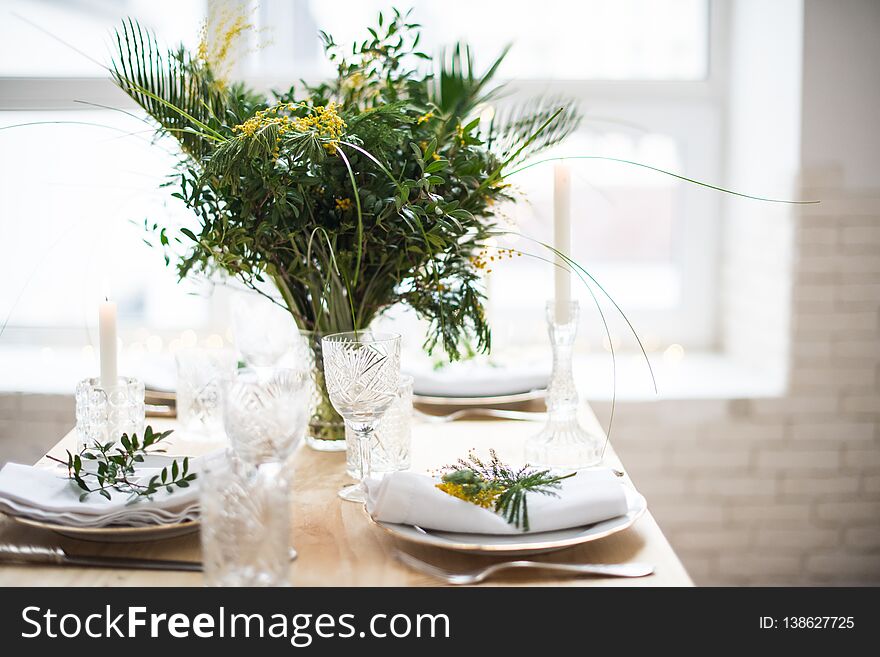 Beautiful springtime table setting with green leaves and mimosa branches, bright white table dinner decoration close-up