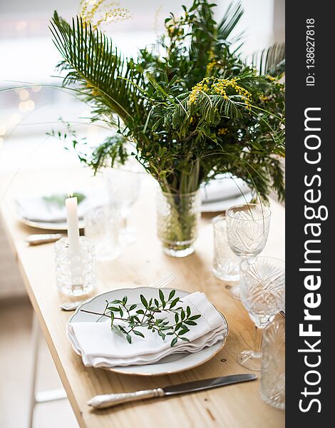 Beautiful springtime table setting with green leaves and mimosa branches, bright white table dinner decoration close-up