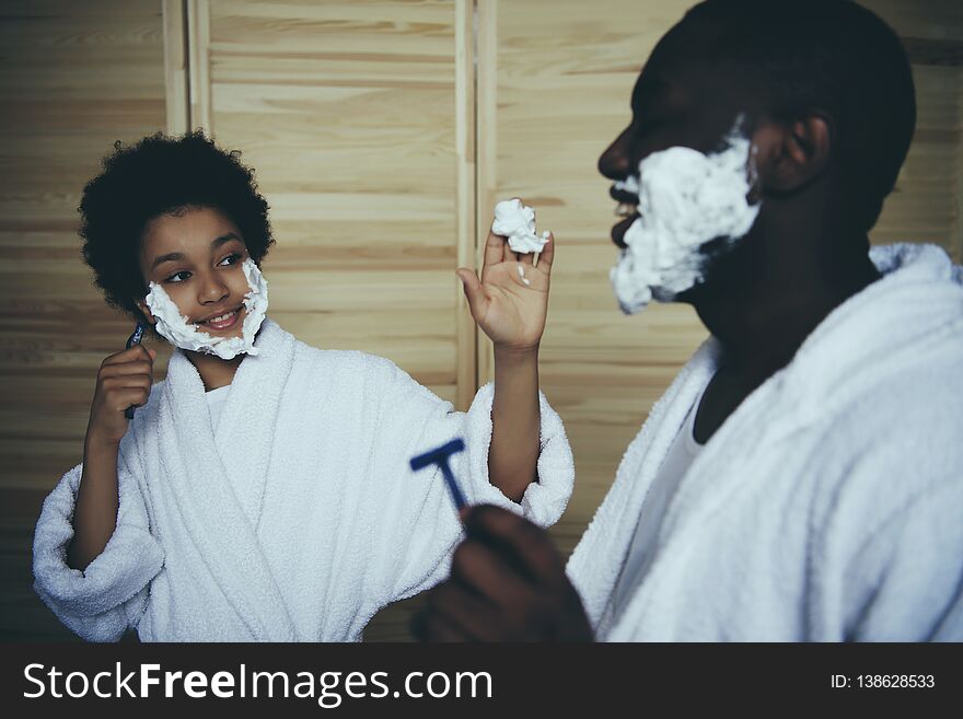 Little black boy stains father with shaving foam. Men traditions. Two generations. Father Day. Fun