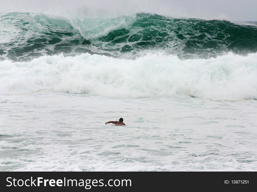 A surfer swimming towards a huge wave in Hawaii.